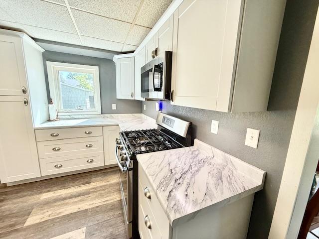 220 Front St E, Redwood Falls, MN 56283 - kitchen featuring appliances with stainless steel finishes, light wood-style floors, white cabinets, light stone counters, and a drop ceiling