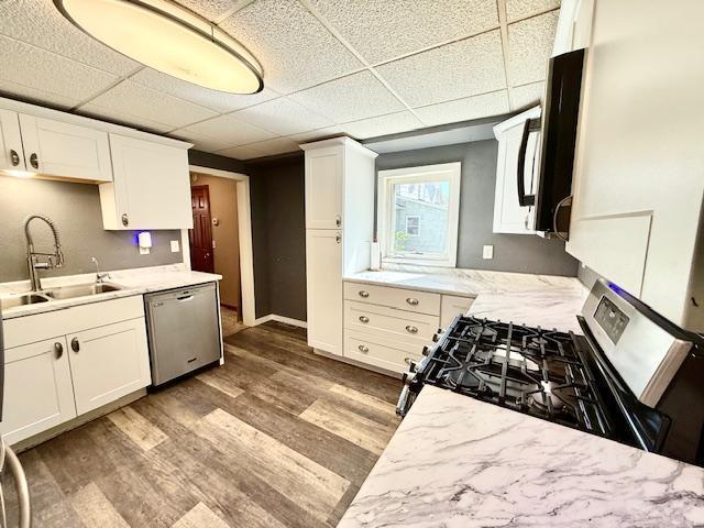 220 Front St E, Redwood Falls, MN 56283 - kitchen featuring appliances with stainless steel finishes, a sink, wood finished floors, a paneled ceiling, and white cabinetry
