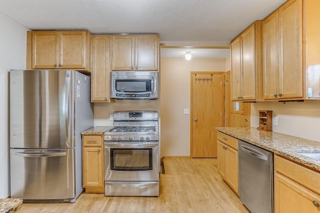 1221 43rd Ave NE, Columbia Heights, MN 55421 - kitchen featuring stainless steel appliances, light wood-style floors, light stone countertops, and a textured ceiling