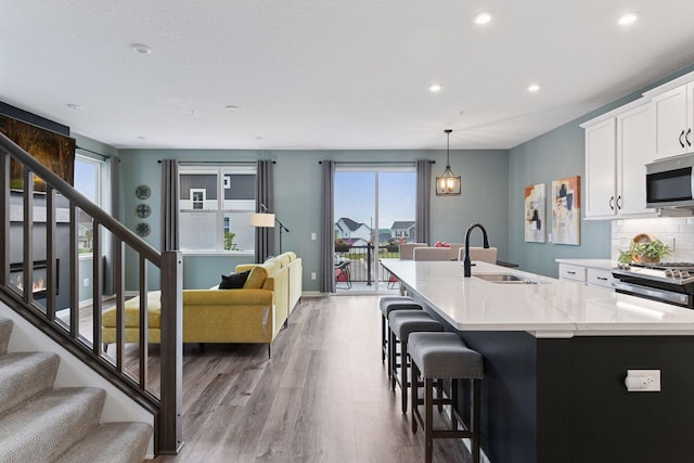 6678 Wildflower Way, Minnetrista, MN 55331 - kitchen featuring appliances with stainless steel finishes, wood finished floors, a center island with sink, recessed lighting, and decorative backsplash