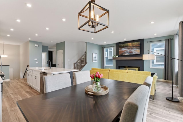 6678 Wildflower Way, Minnetrista, MN 55331 - dining space featuring stairway, light wood-style floors, a glass covered fireplace, a chandelier, and recessed lighting