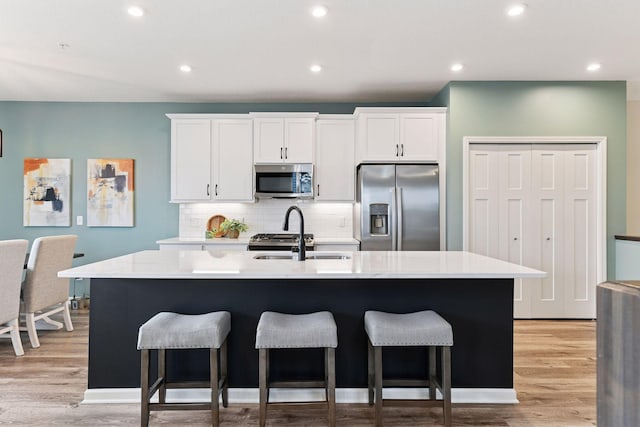 6678 Wildflower Way, Minnetrista, MN 55331 - kitchen with appliances with stainless steel finishes, a kitchen bar, light wood-type flooring, an island with sink, and recessed lighting