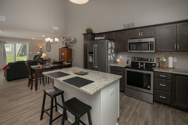1217 Sundance Ct NE, Byron, MN 55920 - kitchen featuring appliances with stainless steel finishes, a towering ceiling, open floor plan, a breakfast bar, and light stone counters
