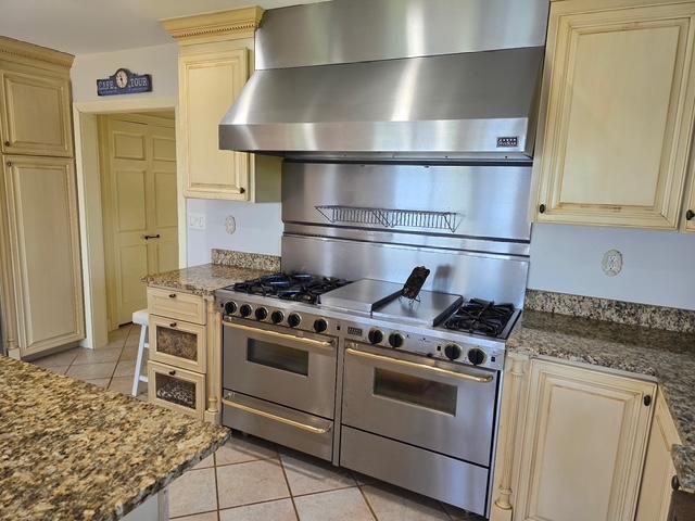 28320 State Highway 65, Pengilly, MN 55775 - kitchen with cream cabinets, light tile patterned floors, wall chimney exhaust hood, and dark stone counters