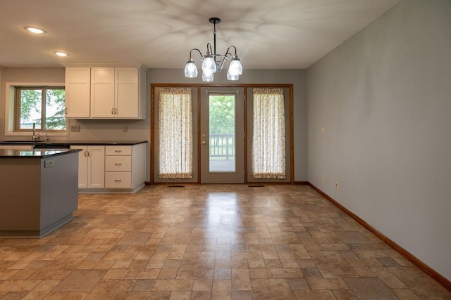 2851 120th Ave SW, Willmar, MN 56201 - kitchen with baseboards, dark countertops, white cabinetry, a chandelier, and light stone finish floors