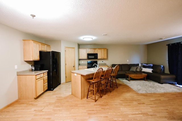 2778 Ridgeview Ln, Red Wing, MN 55066 - kitchen featuring black appliances, light brown cabinetry, light wood-type flooring, open floor plan, and a textured ceiling