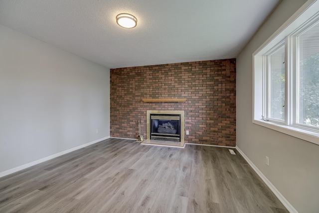4207 Fillmore St NE, Columbia Heights, MN 55421 - unfurnished living room featuring wood finished floors, a brick fireplace, baseboards, brick wall, and a textured ceiling