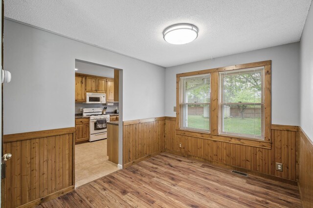 3364 85th Ave, Princeton, MN 55371 - unfurnished dining area featuring wainscoting, wood walls, light wood finished floors, and a textured ceiling