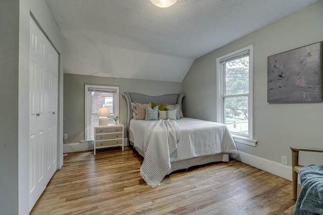 1066 Reaney Ave, Saint Paul, MN 55106 - bedroom featuring light wood-style floors, multiple windows, vaulted ceiling, a textured ceiling, and baseboards