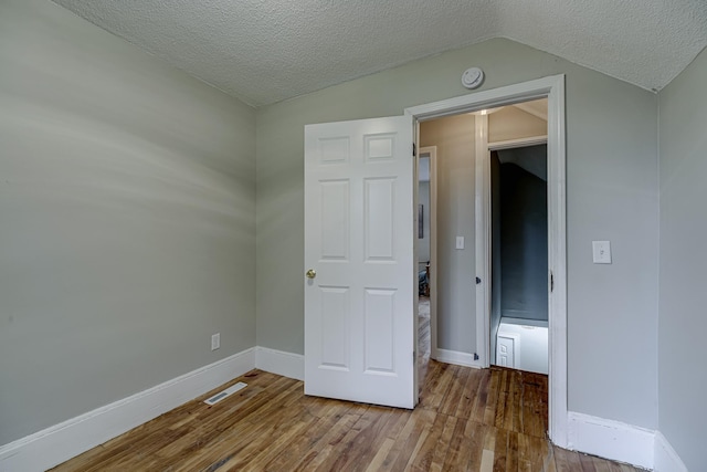 1066 Reaney Ave, Saint Paul, MN 55106 - unfurnished bedroom featuring wood finished floors, a textured ceiling, vaulted ceiling, and baseboards