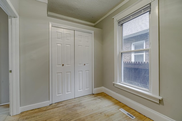 1066 Reaney Ave, Saint Paul, MN 55106 - unfurnished bedroom featuring crown molding, a textured ceiling, light wood-style floors, a closet, and baseboards
