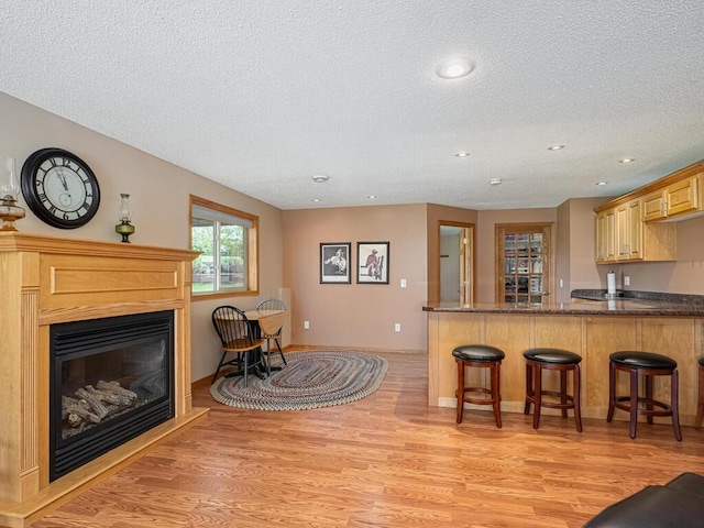 9368 188th Ave NW, Nowthen, MN 55330 - kitchen with a textured ceiling, light wood-type flooring, a kitchen breakfast bar, a glass covered fireplace, and dark stone countertops