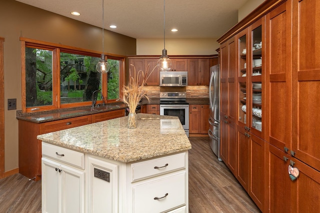 2373 Tee Time Rd SE, Rochester, MN 55904 - kitchen with stainless steel appliances, brown cabinetry, a center island, glass insert cabinets, and light stone countertops