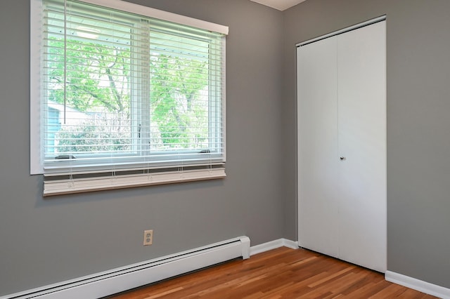 4020 Orleans Ln N, Plymouth, MN 55441 - unfurnished bedroom with a baseboard radiator, a closet, multiple windows, and wood finished floors
