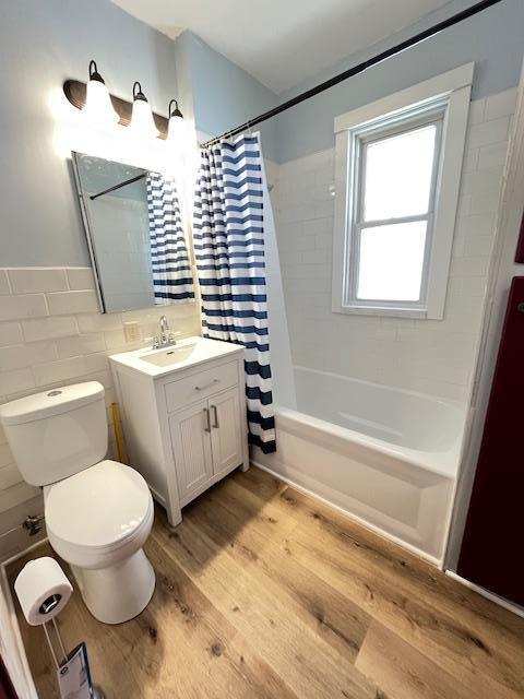 1269 Margaret St, Saint Paul, MN 55106 - bathroom featuring vanity, toilet, shower / bathtub combination with curtain, wood finished floors, and tile walls