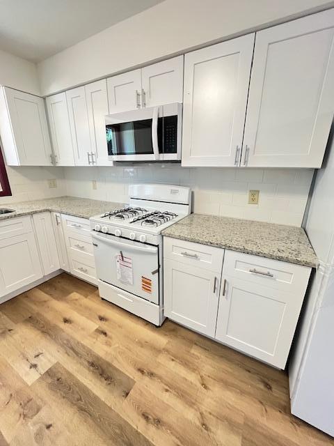 1269 Margaret St, Saint Paul, MN 55106 - kitchen with stainless steel microwave, white range with gas cooktop, white cabinetry, and light wood-style flooring