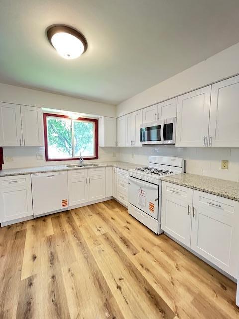 1269 Margaret St, Saint Paul, MN 55106 - kitchen featuring white appliances, a sink, white cabinetry, light wood-style floors, and light stone counters
