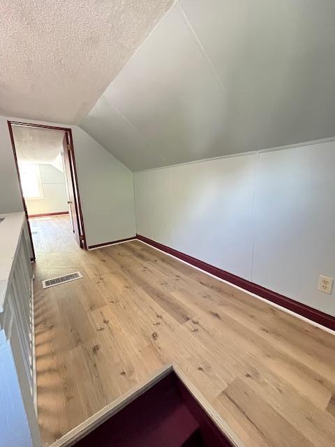 1269 Margaret St, Saint Paul, MN 55106 - additional living space featuring light wood-type flooring, vaulted ceiling, baseboards, and a textured ceiling
