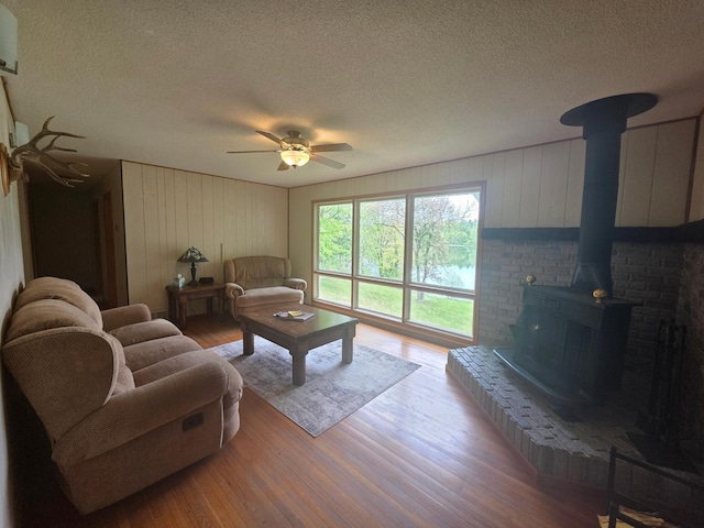 1331 9th St, Grand Rapids, MN 55744 - living room with a textured ceiling, wood finished floors, a wood stove, a ceiling fan, and wooden walls