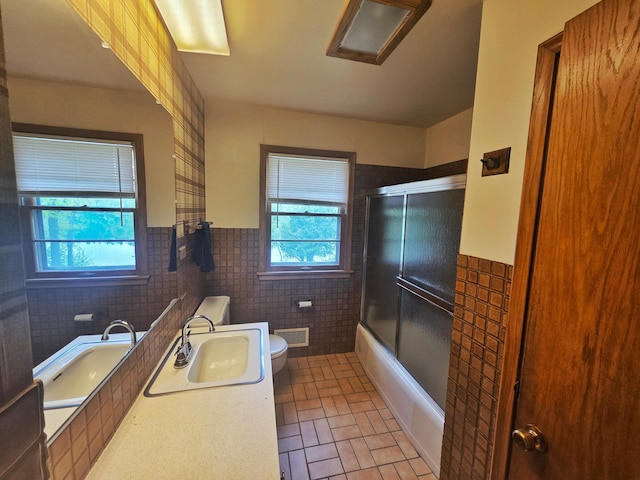1331 9th St, Grand Rapids, MN 55744 - bathroom featuring toilet, tile walls, vanity, wainscoting, and bath / shower combo with glass door
