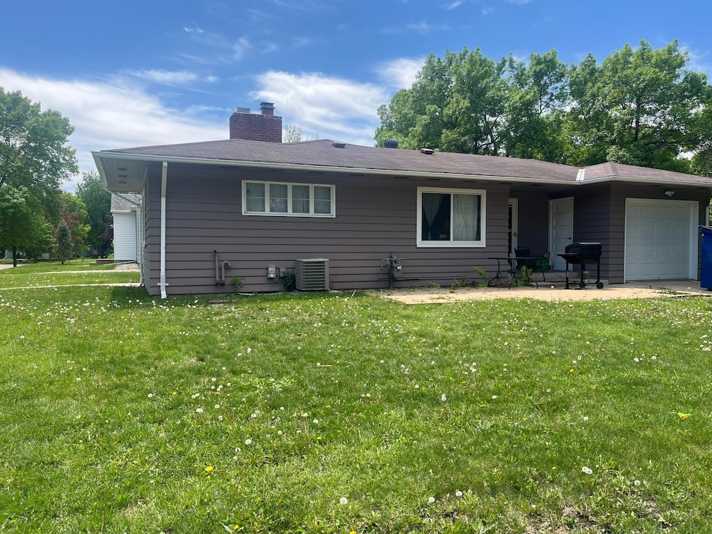 700 14th St SW, Willmar, MN 56201 - rear view of house featuring a garage, cooling unit, a lawn, and a chimney