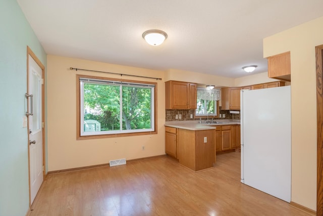 601 4th Ave N, Sauk Rapids, MN 56379 - kitchen featuring freestanding refrigerator, a peninsula, light countertops, light wood-type flooring, and tasteful backsplash