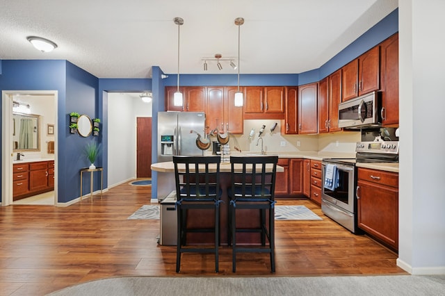 3800 85th Ave N Unit 312, Brooklyn Park, MN 55443 - kitchen featuring appliances with stainless steel finishes, wood finished floors, light countertops, a kitchen breakfast bar, and hanging light fixtures