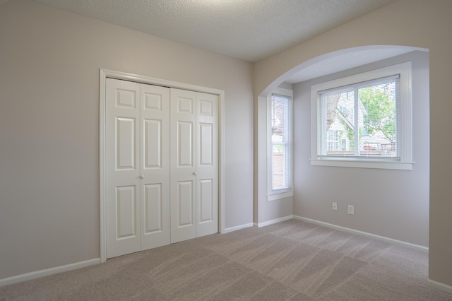 922 Minnehaha Ave E, Saint Paul, MN 55106 - unfurnished bedroom featuring arched walkways, light colored carpet, a closet, baseboards, and a textured ceiling