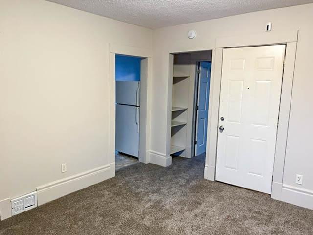310 Burgess St, Saint Paul, MN 55117 - unfurnished bedroom with freestanding refrigerator, dark carpet, baseboards, and a textured ceiling