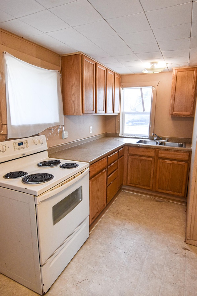 715 8th St E, Thief River Falls, MN 56701 - kitchen featuring electric range, brown cabinetry, a paneled ceiling, light floors, and a sink