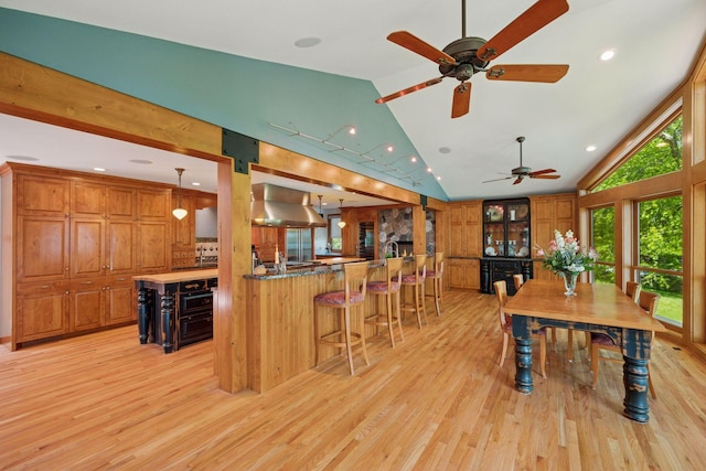4080 Lotus Dr, Minnetrista, MN 55331 - kitchen with wall chimney range hood, lofted ceiling, light wood-style flooring, a kitchen breakfast bar, and brown cabinets