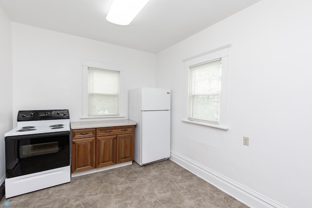 726 College St N, Fargo, ND 58102 - kitchen with freestanding refrigerator, electric range oven, brown cabinetry, light countertops, and baseboards