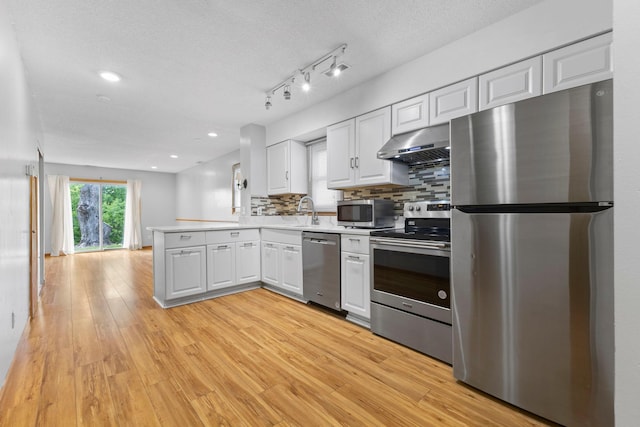 832 Woodgate Dr Unit 107, Vadnais Heights, MN 55127 - kitchen featuring stainless steel appliances, under cabinet range hood, a peninsula, light wood-style flooring, and white cabinetry