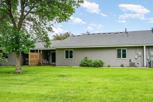 324 7th St NE, New Prague, MN 56071 - back of house featuring a yard, a shingled roof, and central air condition unit