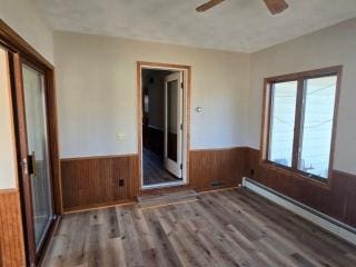 405 16th Ave NE, Waseca, MN 56093 - empty room featuring a wainscoted wall, a baseboard radiator, wood walls, wood finished floors, and a ceiling fan