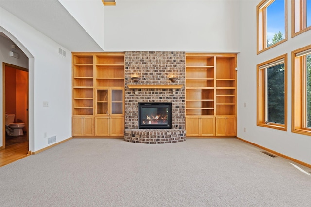 27285 Cambodia Ave, Castle Rock Twp, MN 55024 - unfurnished living room featuring carpet flooring, a brick fireplace, baseboards, built in shelves, and a towering ceiling