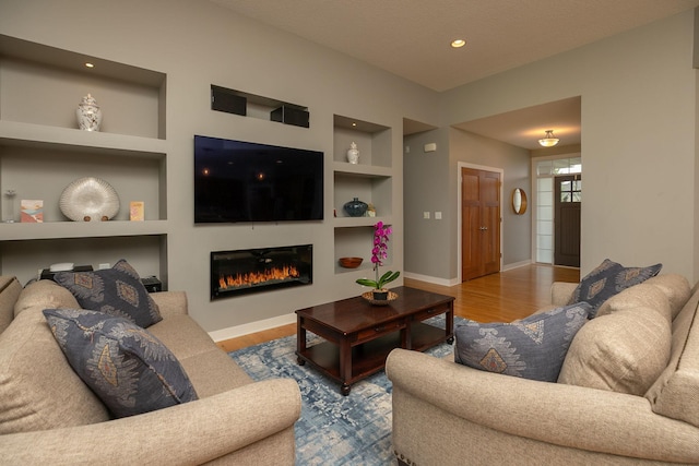 1121 Maplebeck Enclave NE, Byron, MN 55920 - living area with built in features, wood finished floors, baseboards, a glass covered fireplace, and recessed lighting