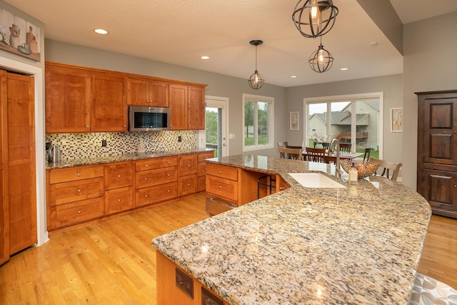 1121 Maplebeck Enclave NE, Byron, MN 55920 - kitchen with stainless steel microwave, a sink, a large island with sink, light wood finished floors, and decorative backsplash