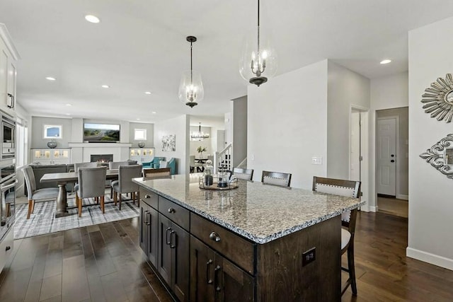 11686 32nd St N, Lake Elmo, MN 55042 - kitchen with a kitchen bar, dark wood-style flooring, light stone countertops, decorative light fixtures, and white cabinetry