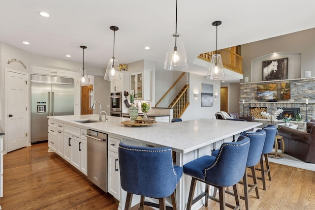 18172 Tamarack Dr, Minnetonka, MN 55345 - kitchen with stainless steel appliances, a sink, a stone fireplace, light wood-type flooring, and a large island with sink