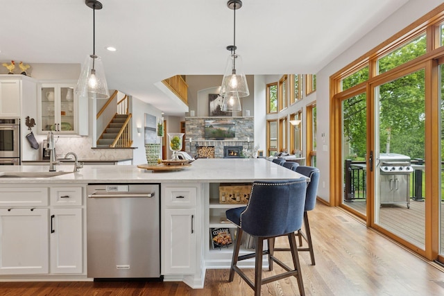 18172 Tamarack Dr, Minnetonka, MN 55345 - kitchen with stainless steel dishwasher, backsplash, a sink, a stone fireplace, and white cabinetry