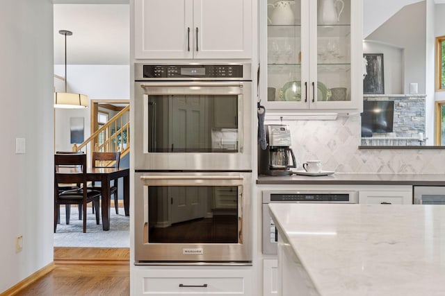 18172 Tamarack Dr, Minnetonka, MN 55345 - kitchen featuring stainless steel double oven, wood finished floors, white cabinets, backsplash, and glass insert cabinets