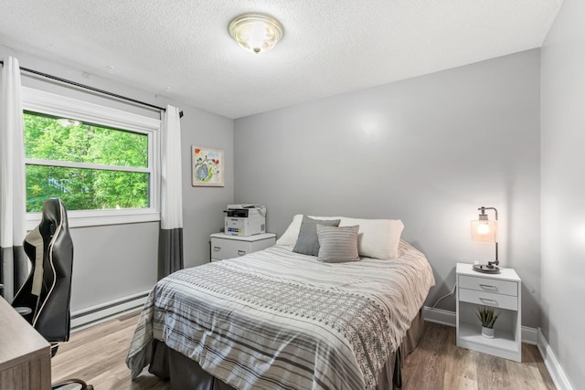 8150 Wildwood Rd, Laketown Twp, MN 55387 - bedroom featuring a baseboard heating unit, light wood-style flooring, a textured ceiling, and baseboards