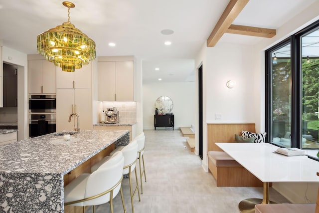 kitchen featuring double wall oven, light stone counters, a chandelier, pendant lighting, and a sink
