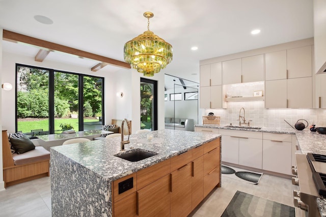kitchen with a sink, decorative backsplash, a kitchen island with sink, pendant lighting, and beam ceiling