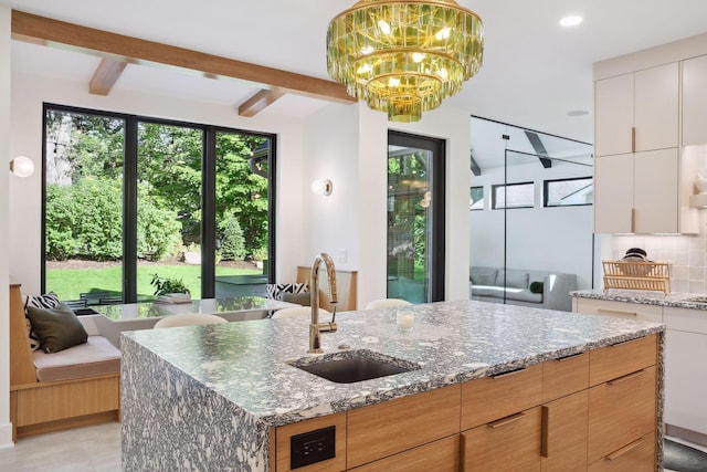 kitchen featuring a sink, healthy amount of natural light, beam ceiling, tasteful backsplash, and stone counters