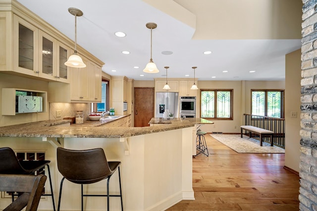 451 Reflection Rd, Apple Valley, MN 55124 - kitchen featuring appliances with stainless steel finishes, cream cabinets, light stone counters, a kitchen bar, and a peninsula