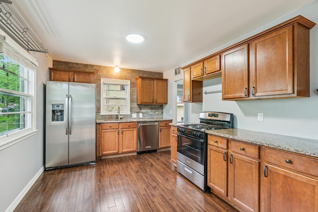 3945 15th Ave S, Minneapolis, MN 55407 - kitchen with appliances with stainless steel finishes, brown cabinets, light stone countertops, dark wood-style flooring, and a sink