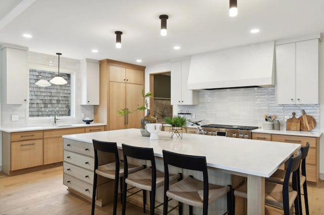 kitchen featuring a sink, custom exhaust hood, light countertops, a breakfast bar, and decorative backsplash