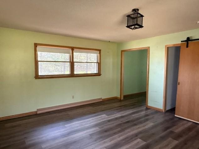 510 2nd Ave NW, Milaca, MN 56353 - unfurnished bedroom featuring a barn door, dark wood-style flooring, and baseboards